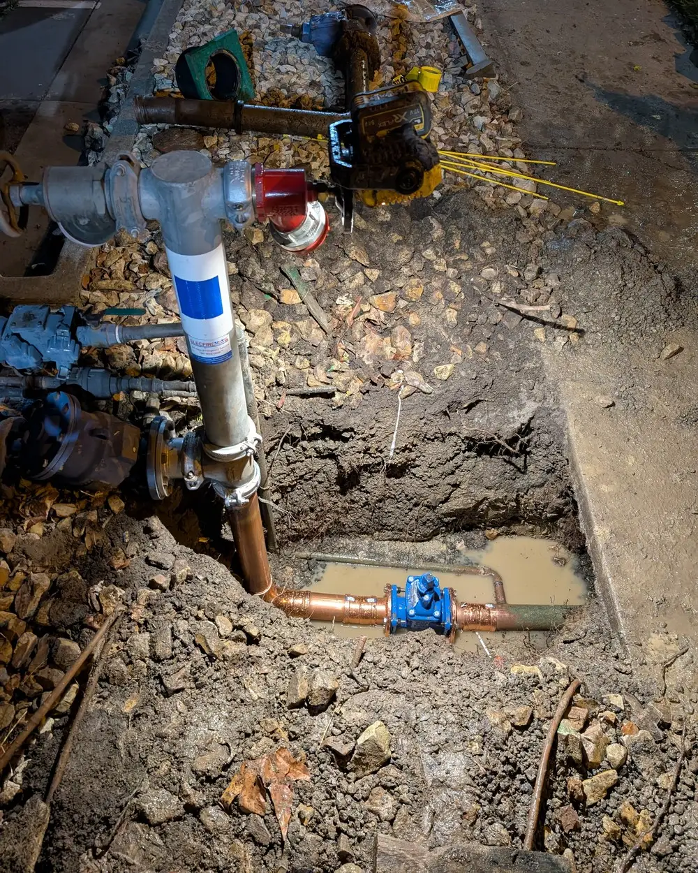 A fire service riser repaired at night, with new copper pipe and a blue valve in the excavation