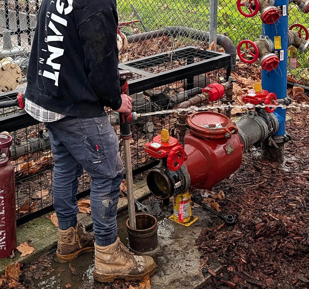 Fire booster assembly repair in Melbourne, a Giant Plumbing team member at the red valves inside the booster cage