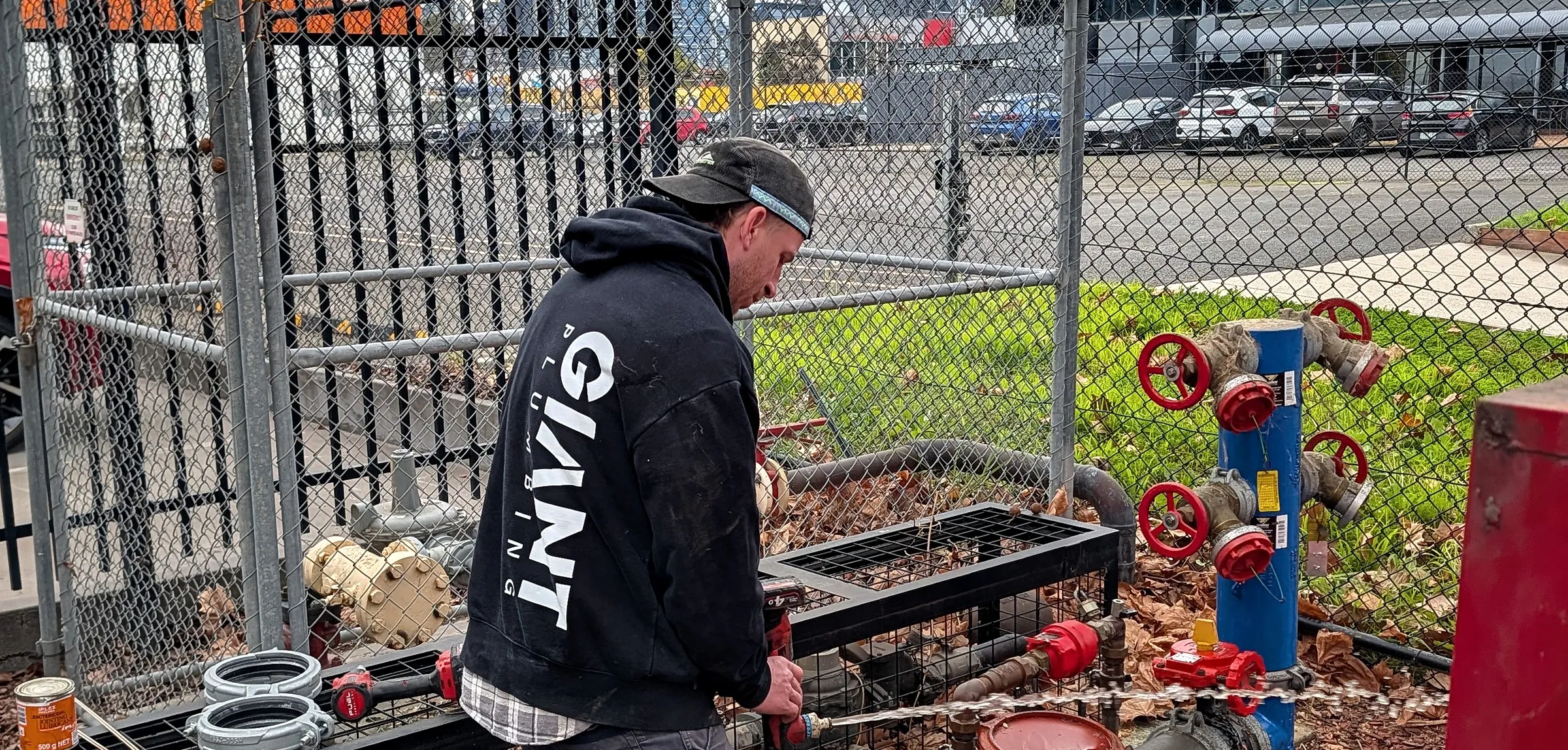 A Giant Plumbing team member repairs a caged fire booster assembly with red valves on an industrial site