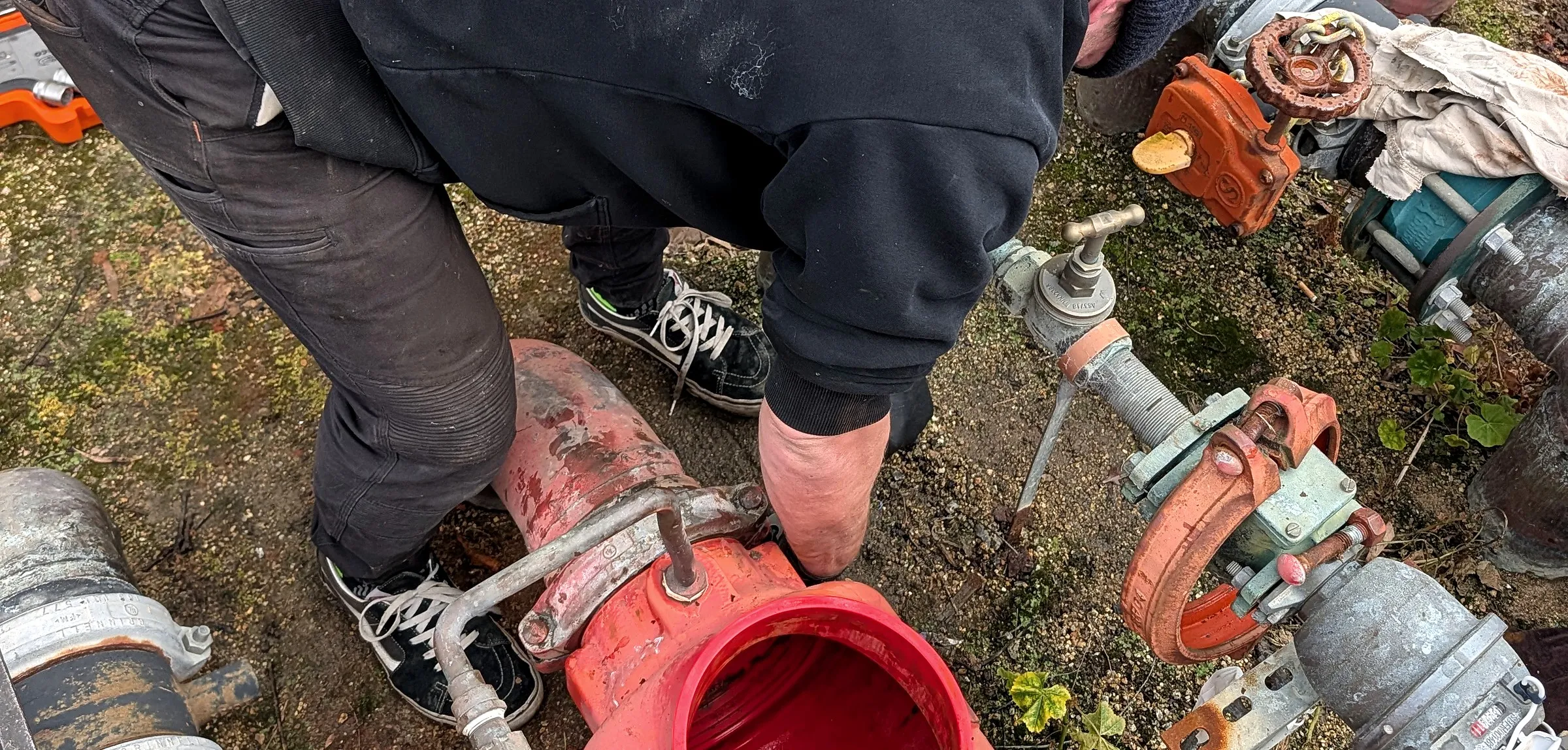 A Giant Plumbing team member works on a cut section of red fire main with a new coupling and valve in a grassed pit