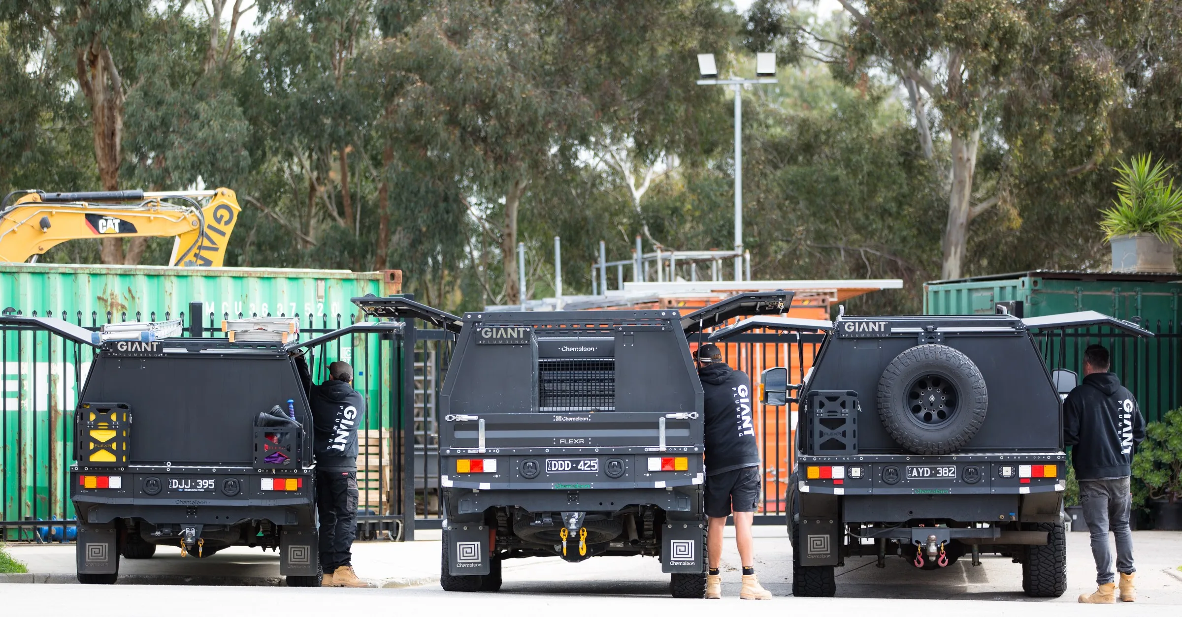 Giant Plumbing team members at the open tool canopies of three branded utes at the Coburg North yard