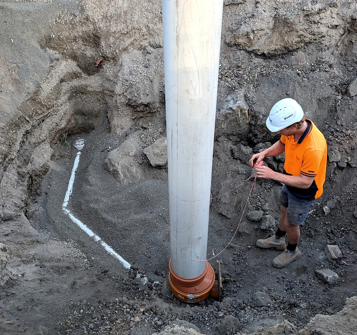 Deep rock excavation in Melbourne for a large PVC drainage riser, a Giant Plumbing worker beside it