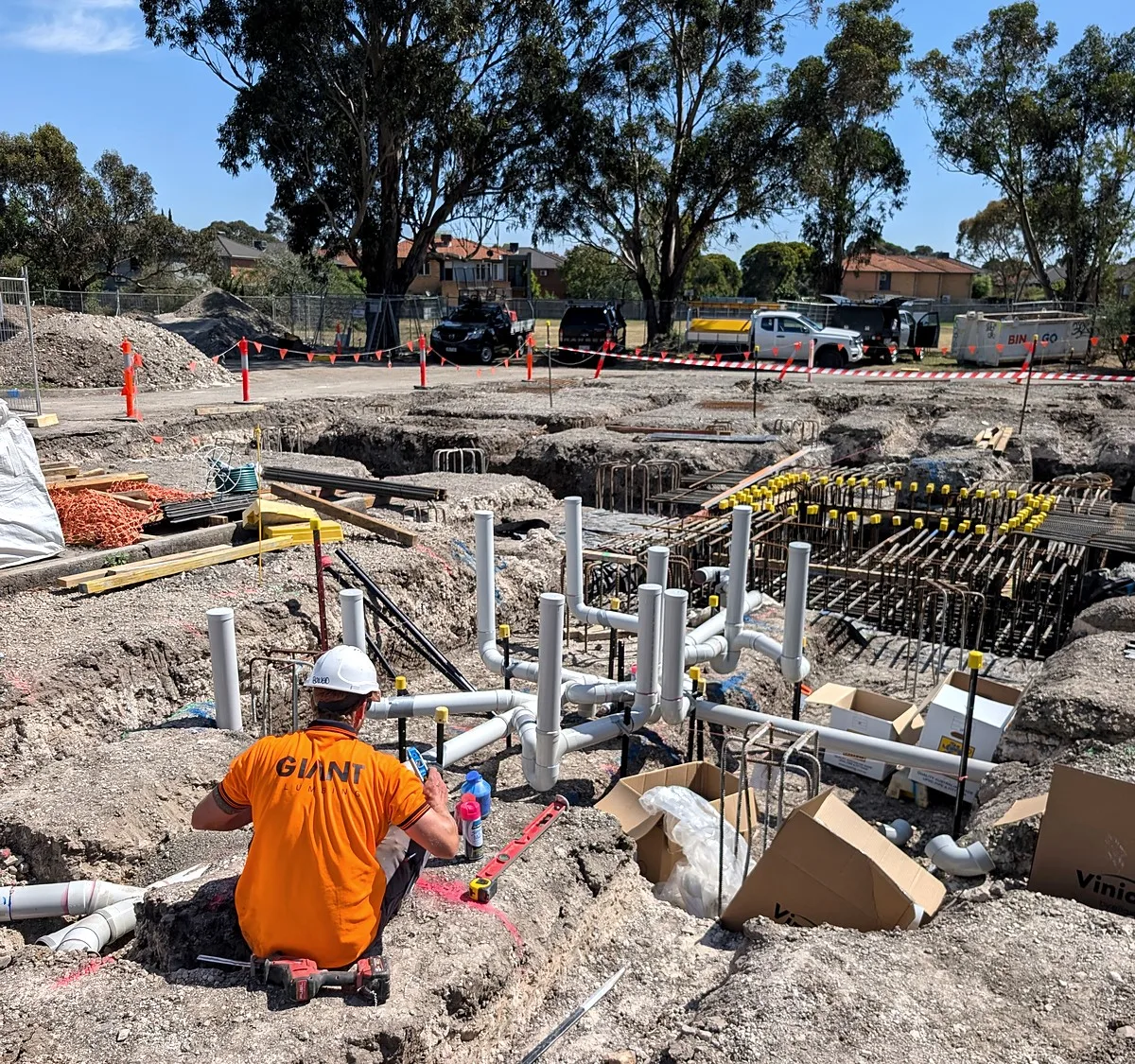 Commercial drainage excavation on a Melbourne building site, a Giant Plumbing team member among the pile cages and pipe stubs