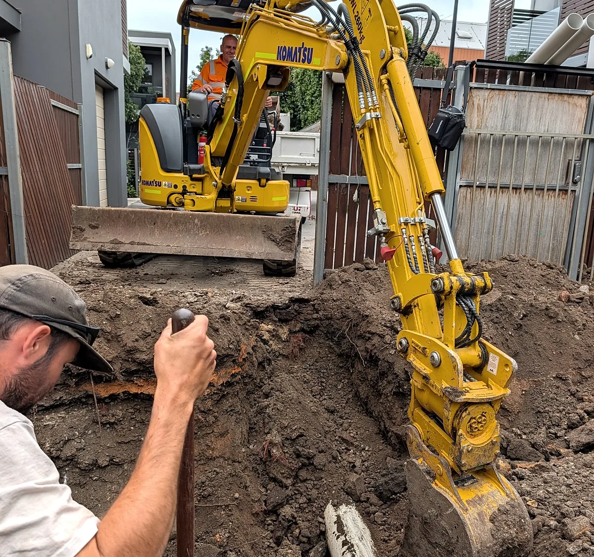Trenching in Melbourne with a Giant Plumbing excavator, a worker digging beside the bucket