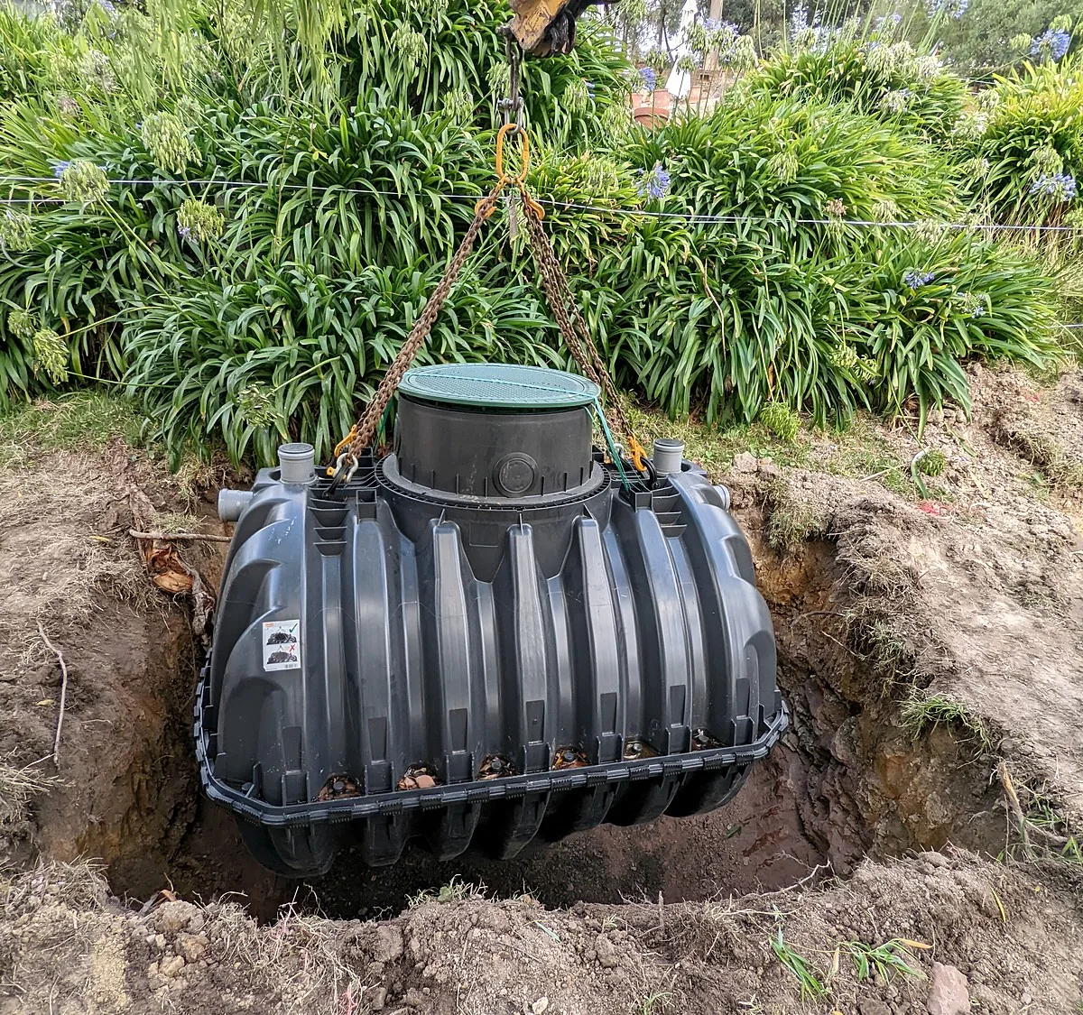 Drainage and stormwater excavation in Melbourne, a poly tank lowered on chains into the dug hole beside a garden bed