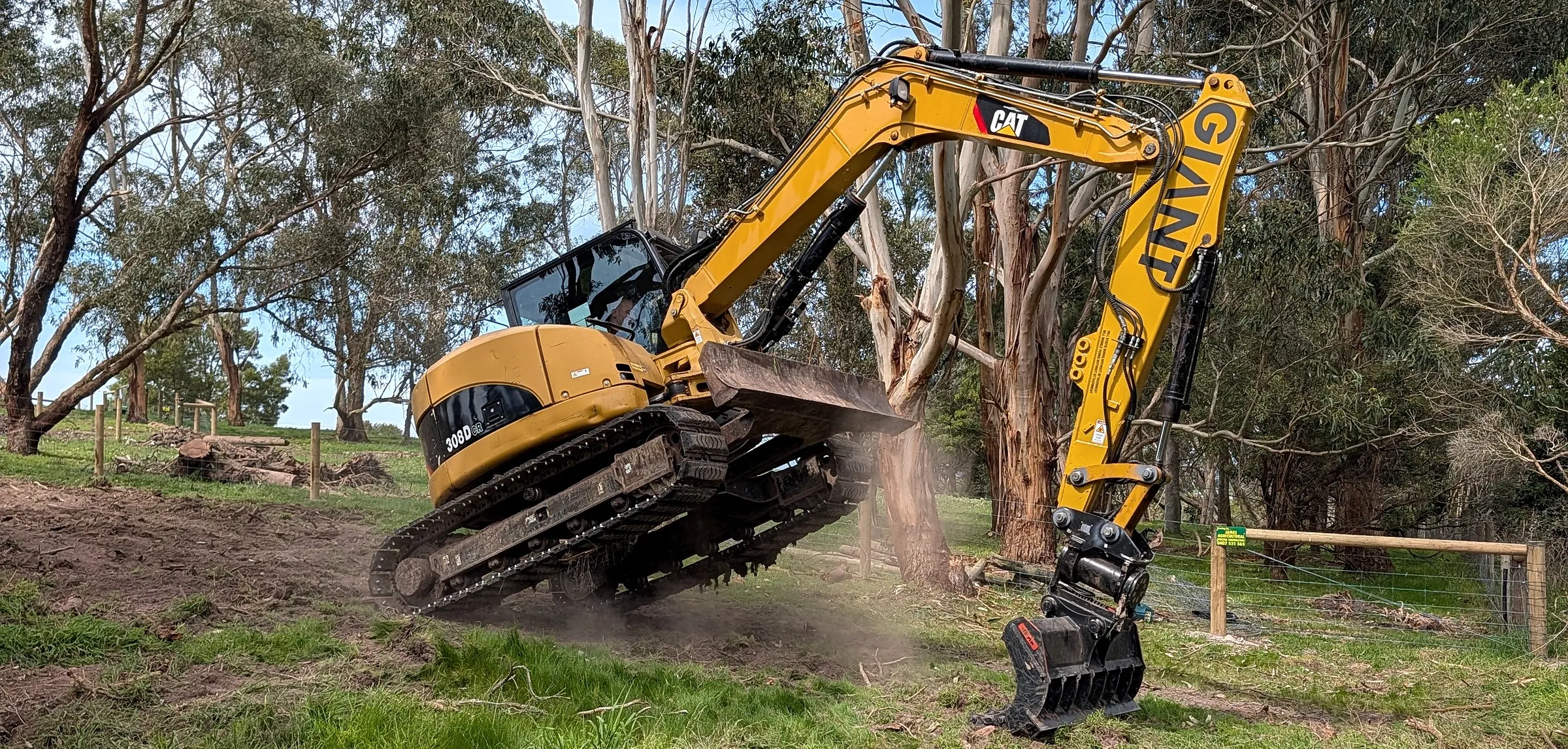 Giant Plumbing's 8 tonne excavator, GIANT on its boom, levelling ground on a site among gum trees