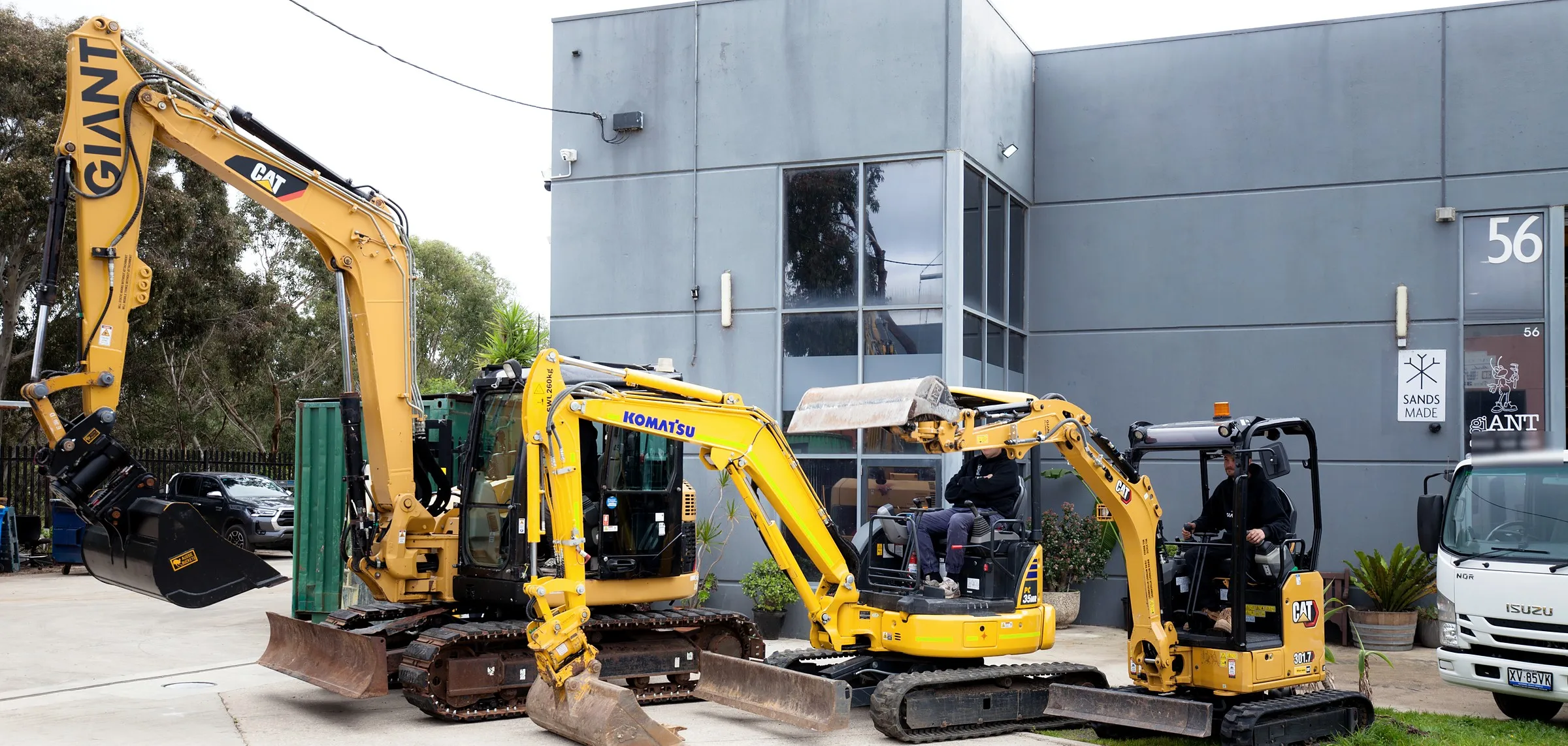 Giant Plumbing's three excavators lined up outside the Coburg North workshop, GIANT on the boom of the 8 tonne CAT, operators in the two smaller machines