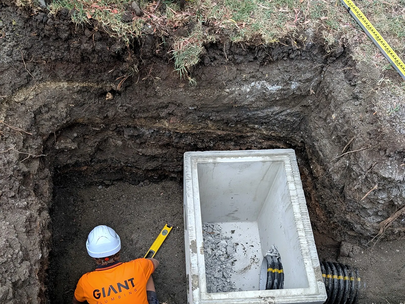 A precast concrete pit lowered into the dig, a Giant Plumbing team member checking its level