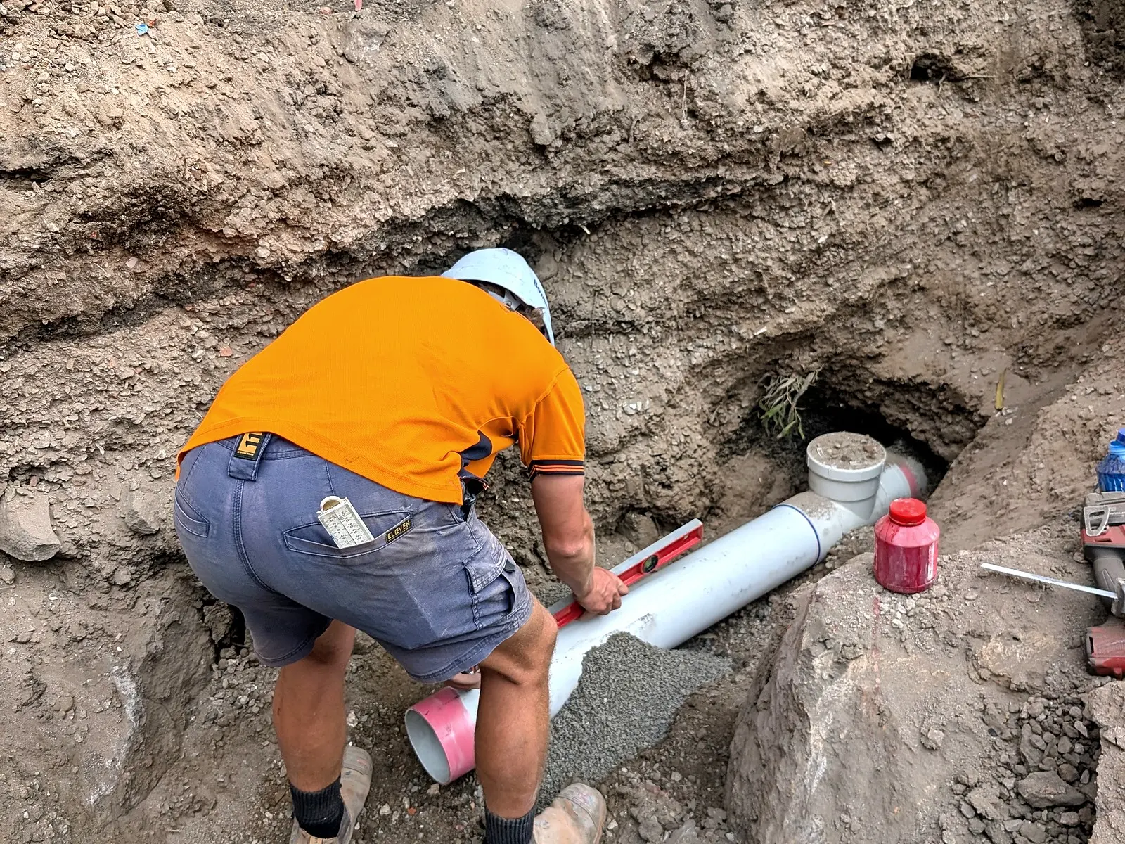 A Giant Plumbing team member lays new PVC sewer pipe in bedding gravel at the bottom of a deep dig