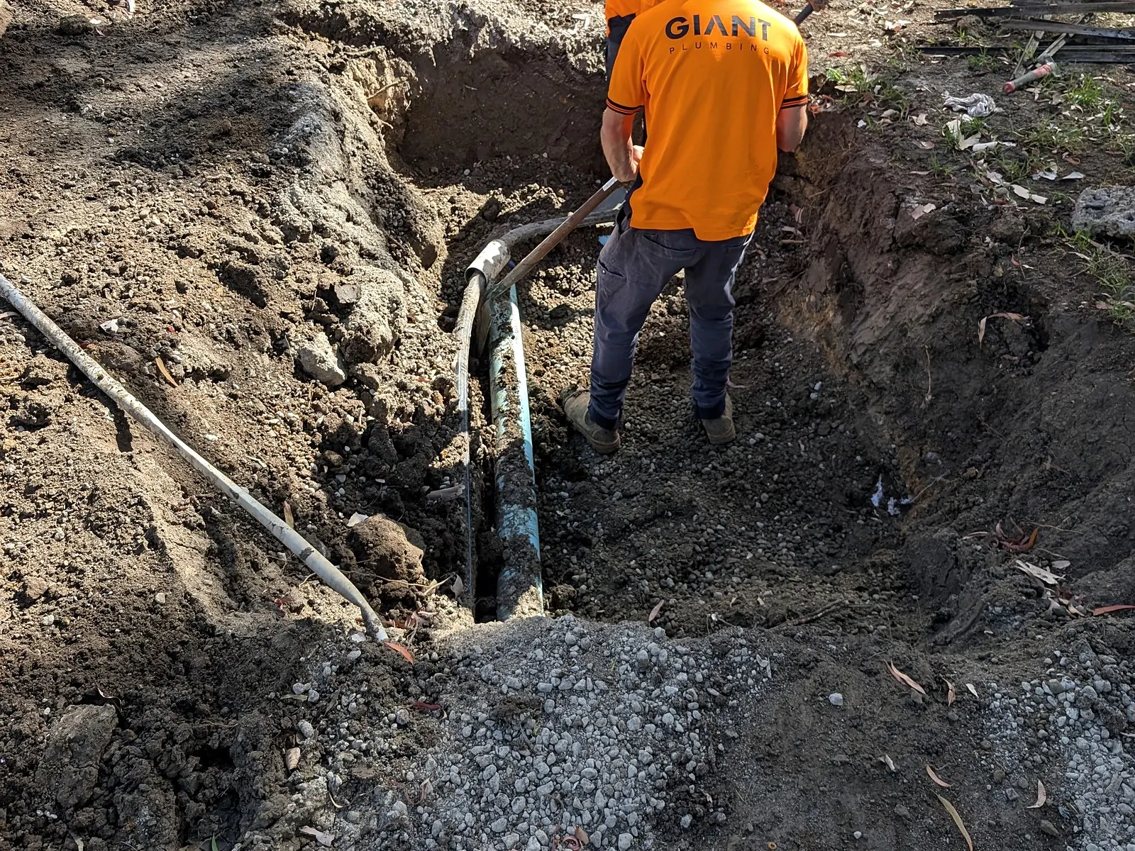 A Giant Plumbing worker exposes an old cast iron pipe by hand in an excavation