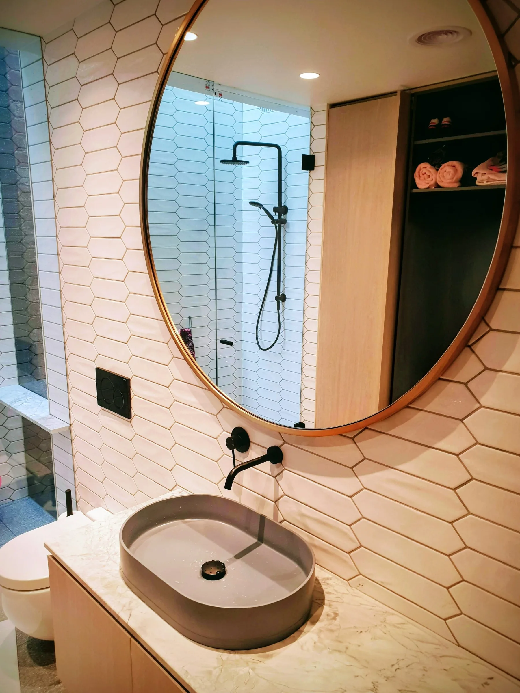 Bathroom basin and round mirror beside a tiled shower