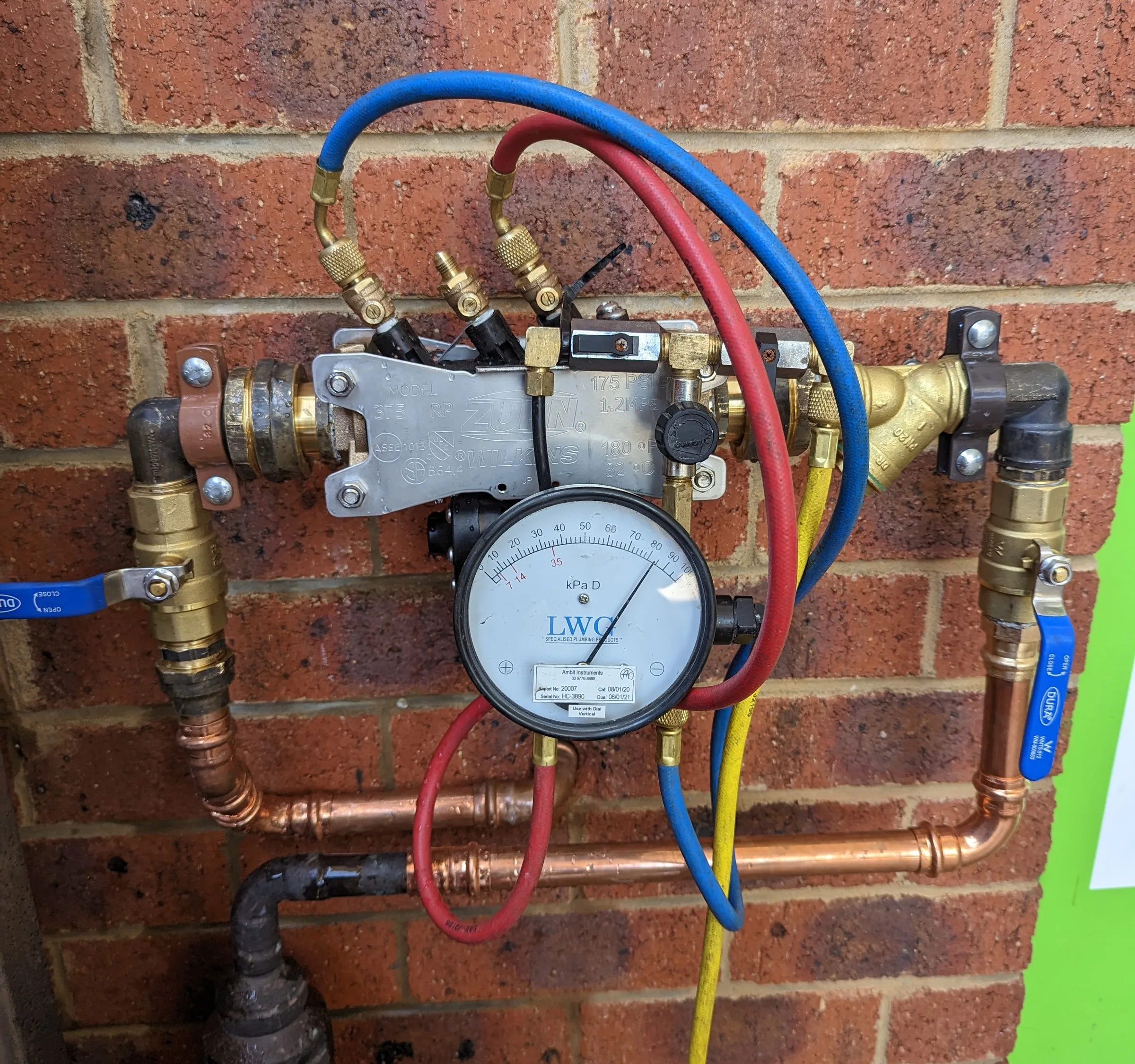 Backflow prevention device being tested with a gauge on a brick wall