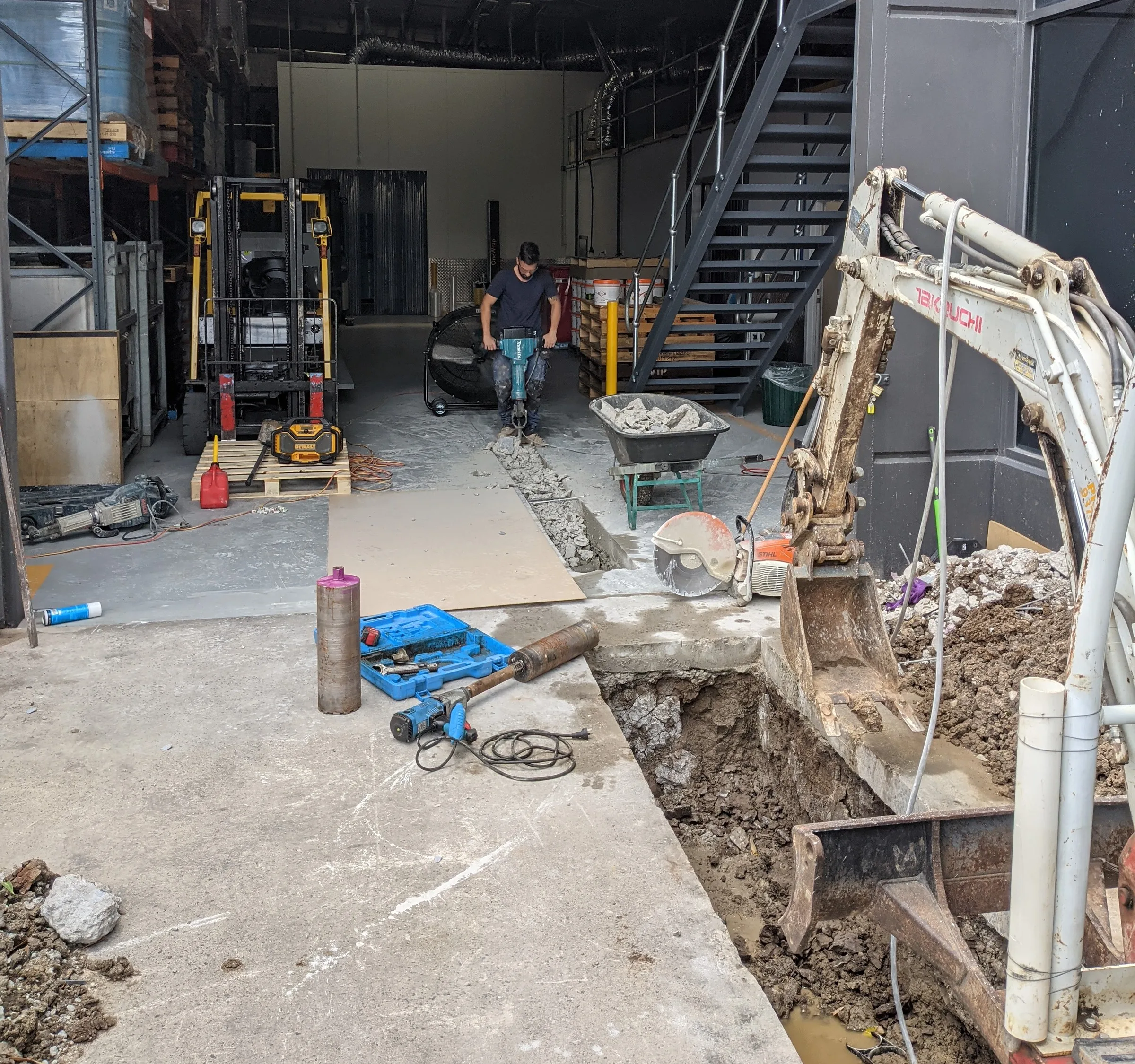 Mini excavator digging a trench through the concrete floor of an industrial unit