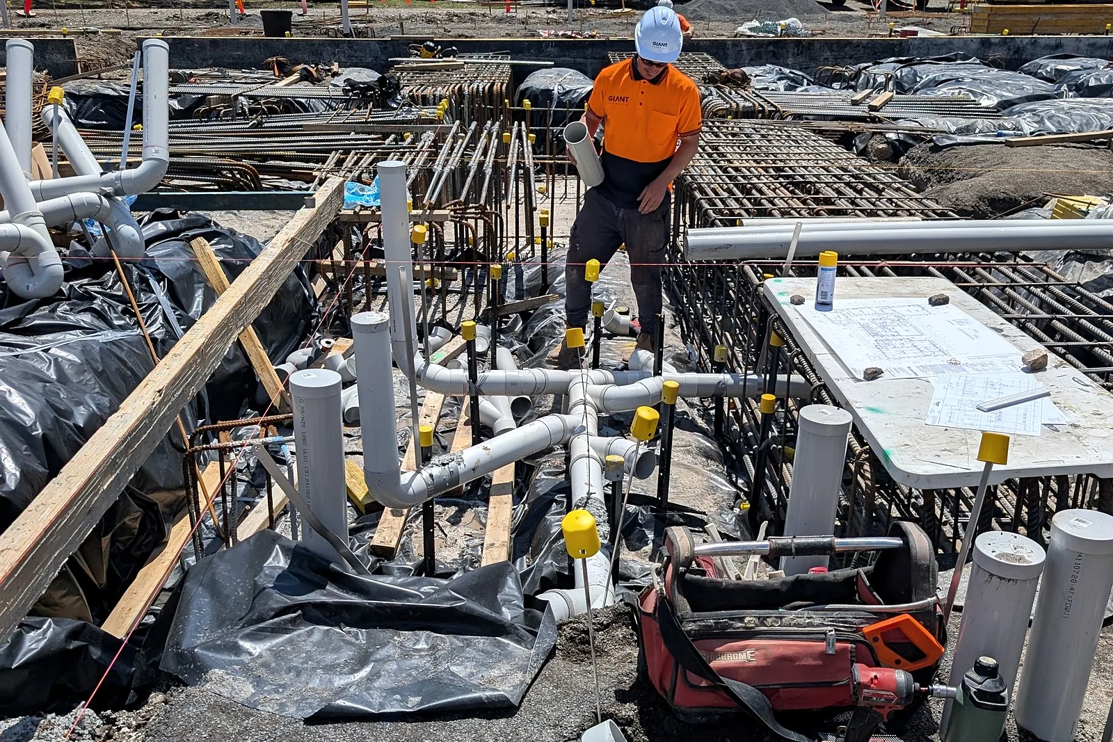 A Giant Plumbing team member in a branded hard hat and shirt among new PVC drainage and reinforcing on a commercial slab