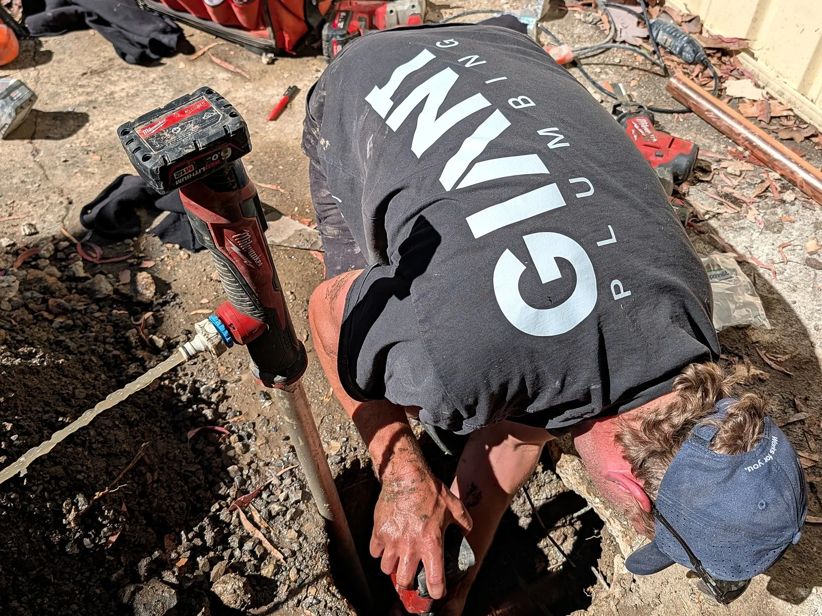 A Giant Plumbing team member digs out a wet pit by hand in a home's side passage while a pump clears the water