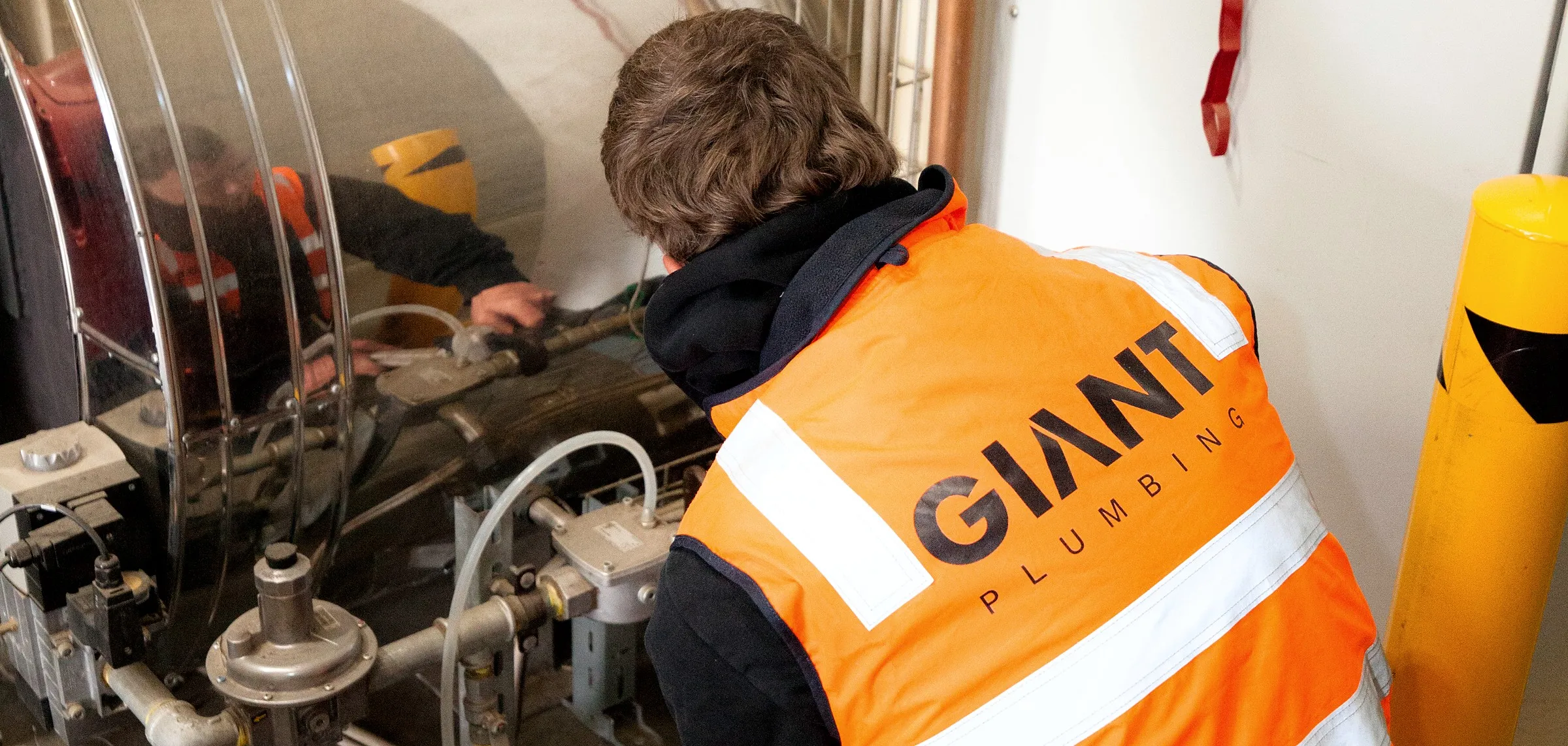 A Giant Plumbing technician in a branded hi-vis vest works on the gas train of an industrial burner