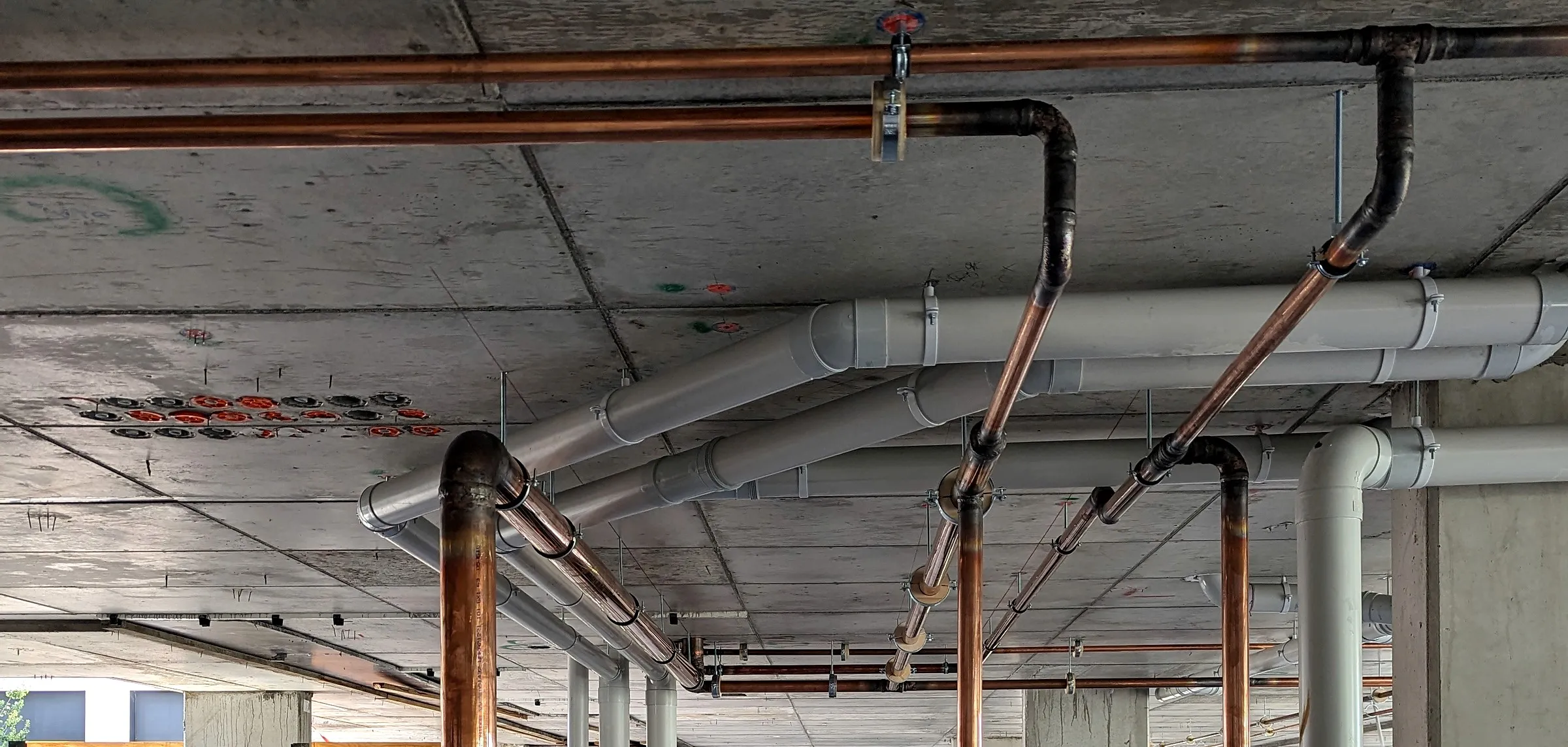 New copper water pipes and grey PVC pipes run under the concrete slab of a commercial building