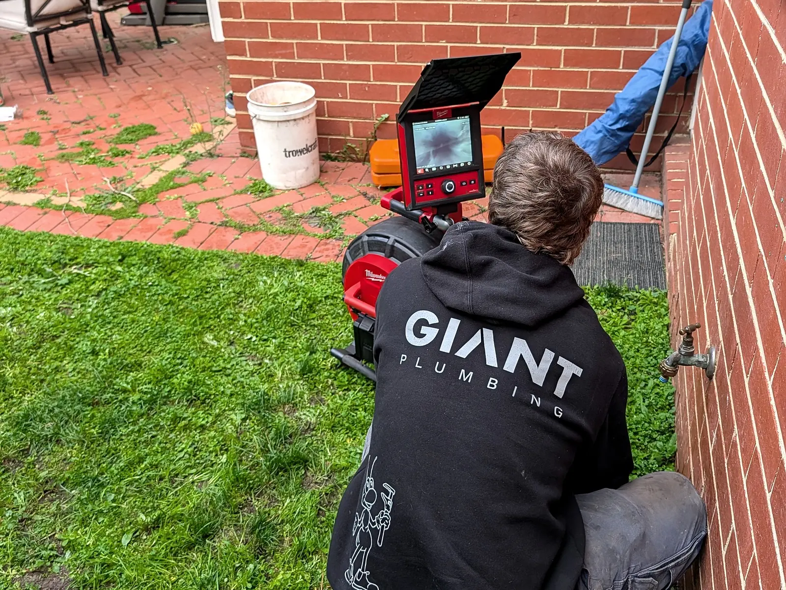 A Giant Plumbing team member in a branded hoodie sets up the drain camera at a house