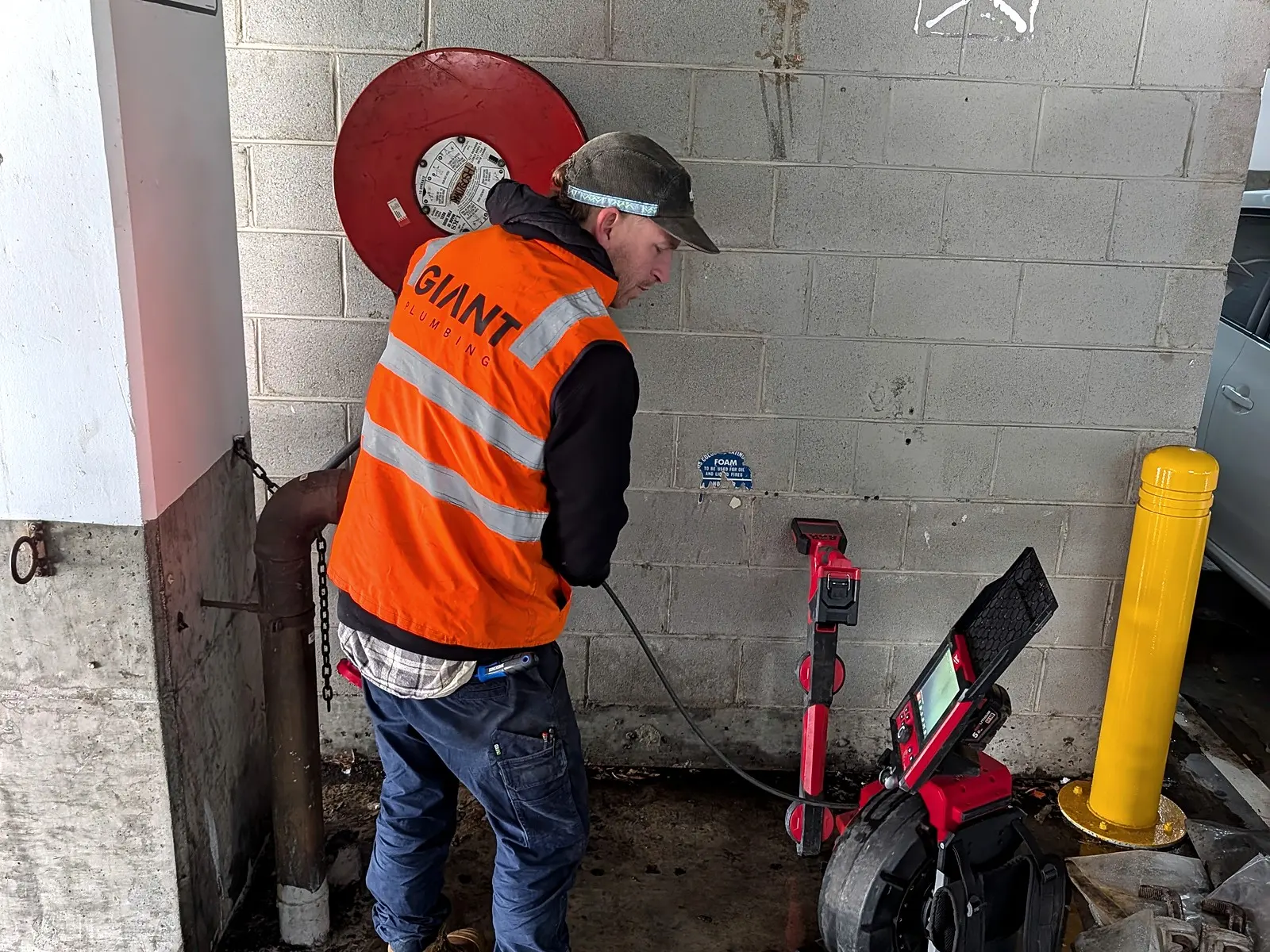 A Giant Plumbing team member in hi-vis runs the drain camera reel into a wall penetration in a car park