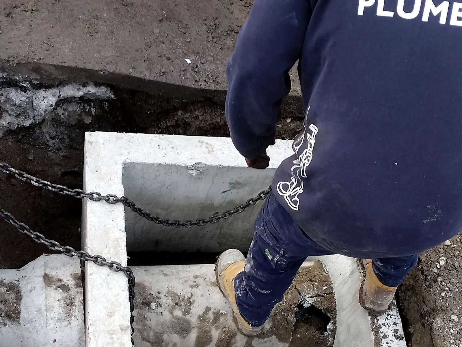 A Giant Plumbing team member steps across a new concrete drainage pit with pipes connected