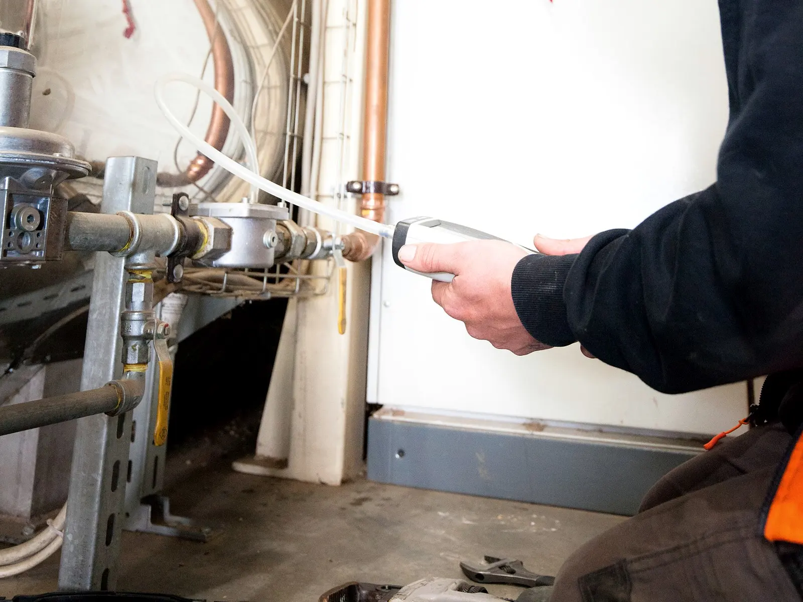 A technician checks the gas pressure at an industrial burner with a handheld digital gauge