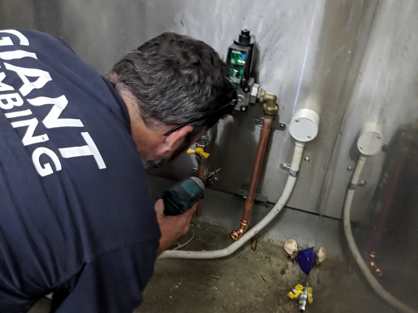 A Giant Plumbing technician works on copper gas pipework below a gas valve against a stainless steel wall