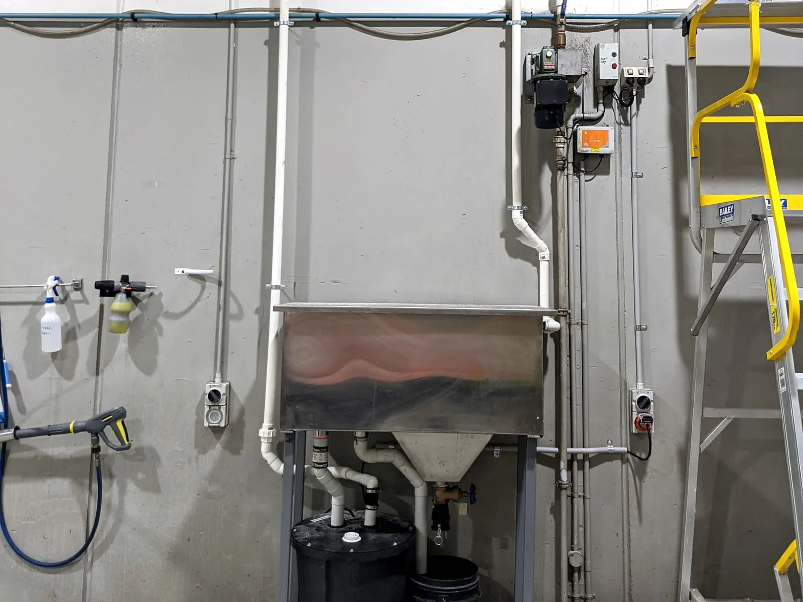 A stainless wash-down trough with its drainage and water pipework on a factory wall
