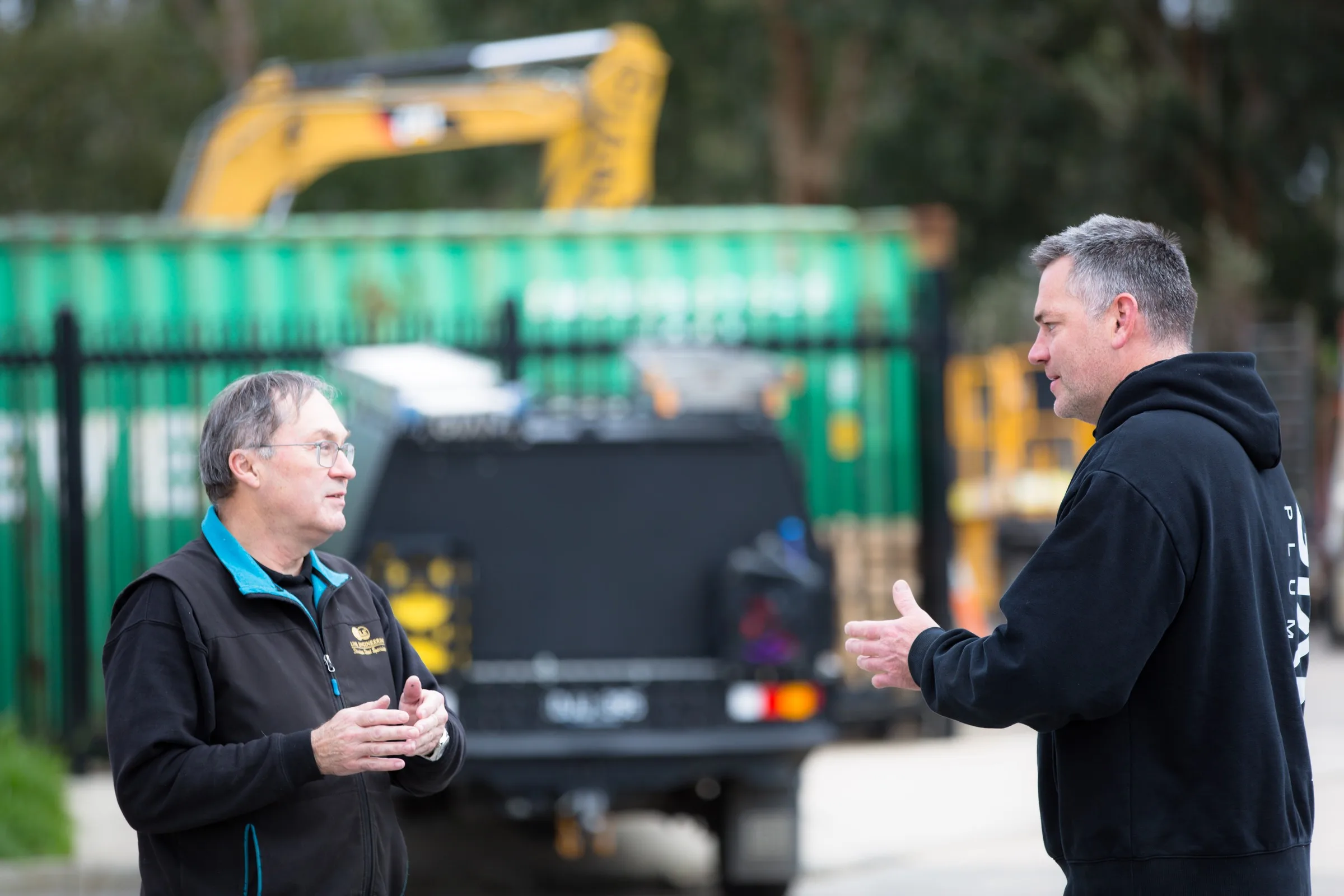 Two Giant Plumbing team members talking beside the work vehicles