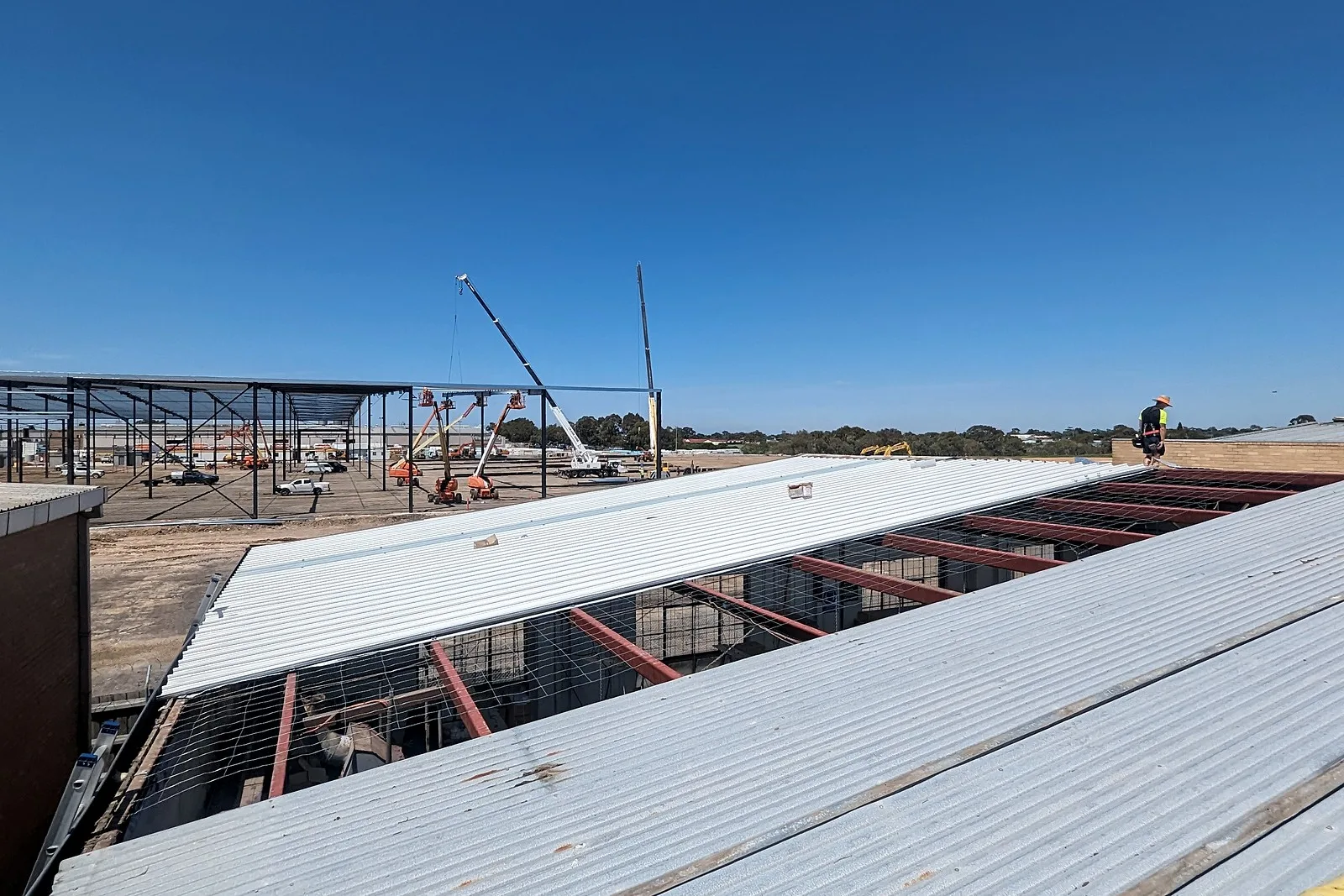 New metal roof sheets laid over safety mesh and purlins on a large industrial roof, a steel structure rising behind