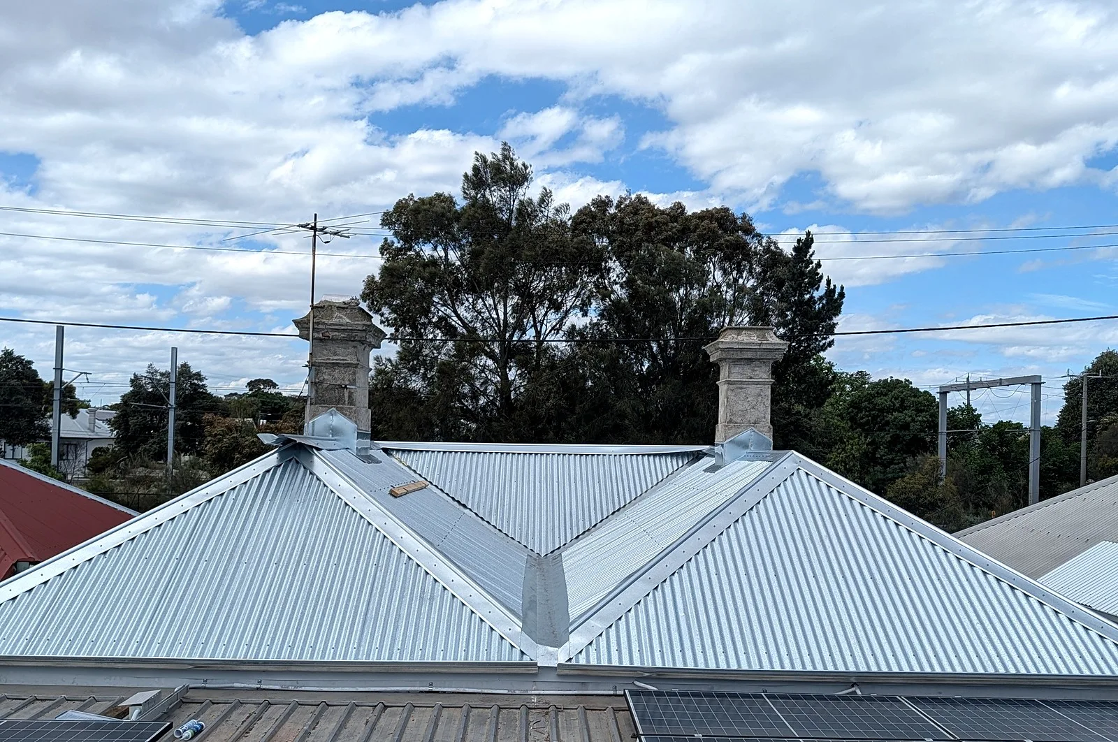 A finished grey metal hip roof with two chimneys on an older Melbourne house, seen from the roof next door