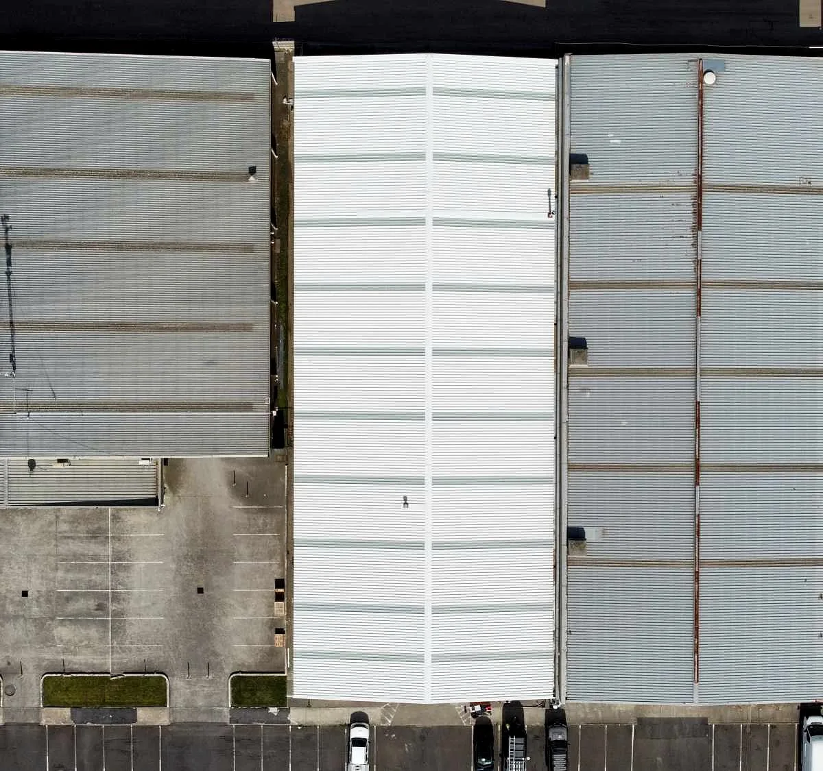 Commercial re-roof in Melbourne by Giant Plumbing, a new white metal roof section between two older factory roofs, seen from above