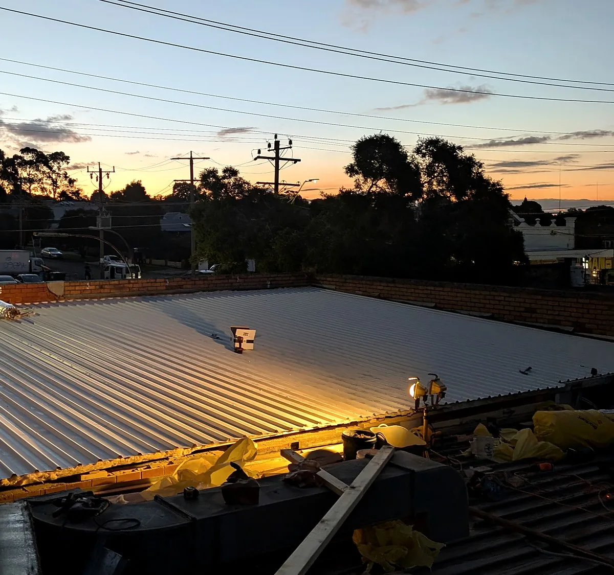 New metal roof sheets laid across a wide commercial roof at sunset on a Melbourne re-roof by Giant Plumbing