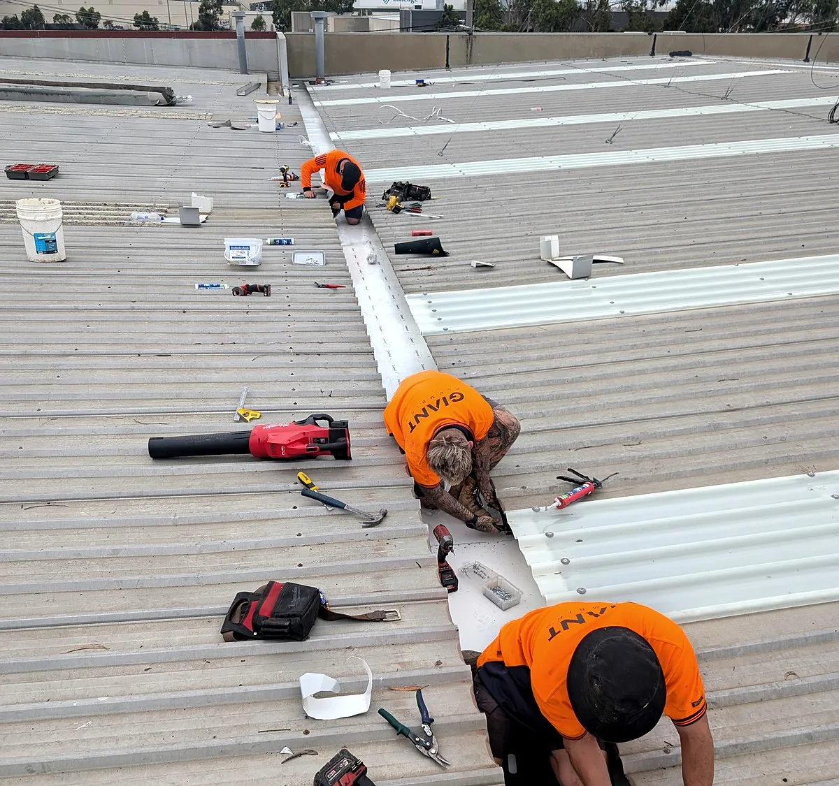 Two Giant Plumbing team members screwing down new metal sheets on a commercial roof in Melbourne