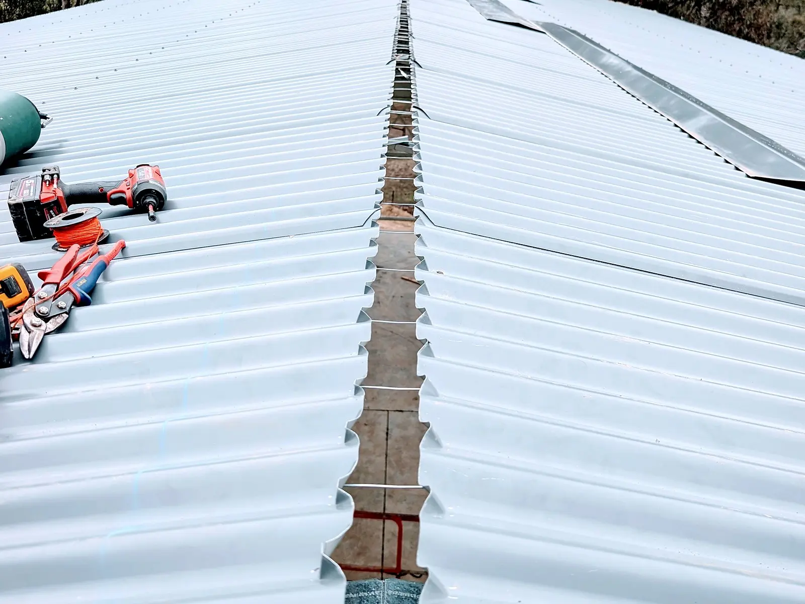 The open ridge of a large shed roof ready for its capping, snips and rivets beside it