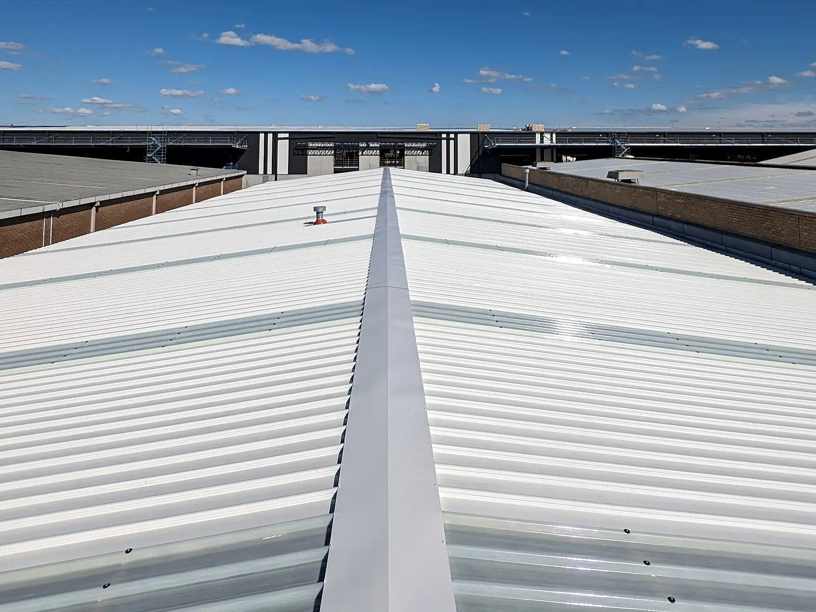 The ridge of a new white metal roof with a flashed vent, an industrial building beyond