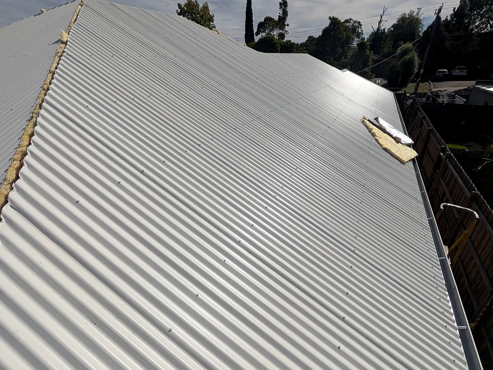 New corrugated metal roof sheets laid down a hip on a house re-roof, the insulation edge showing