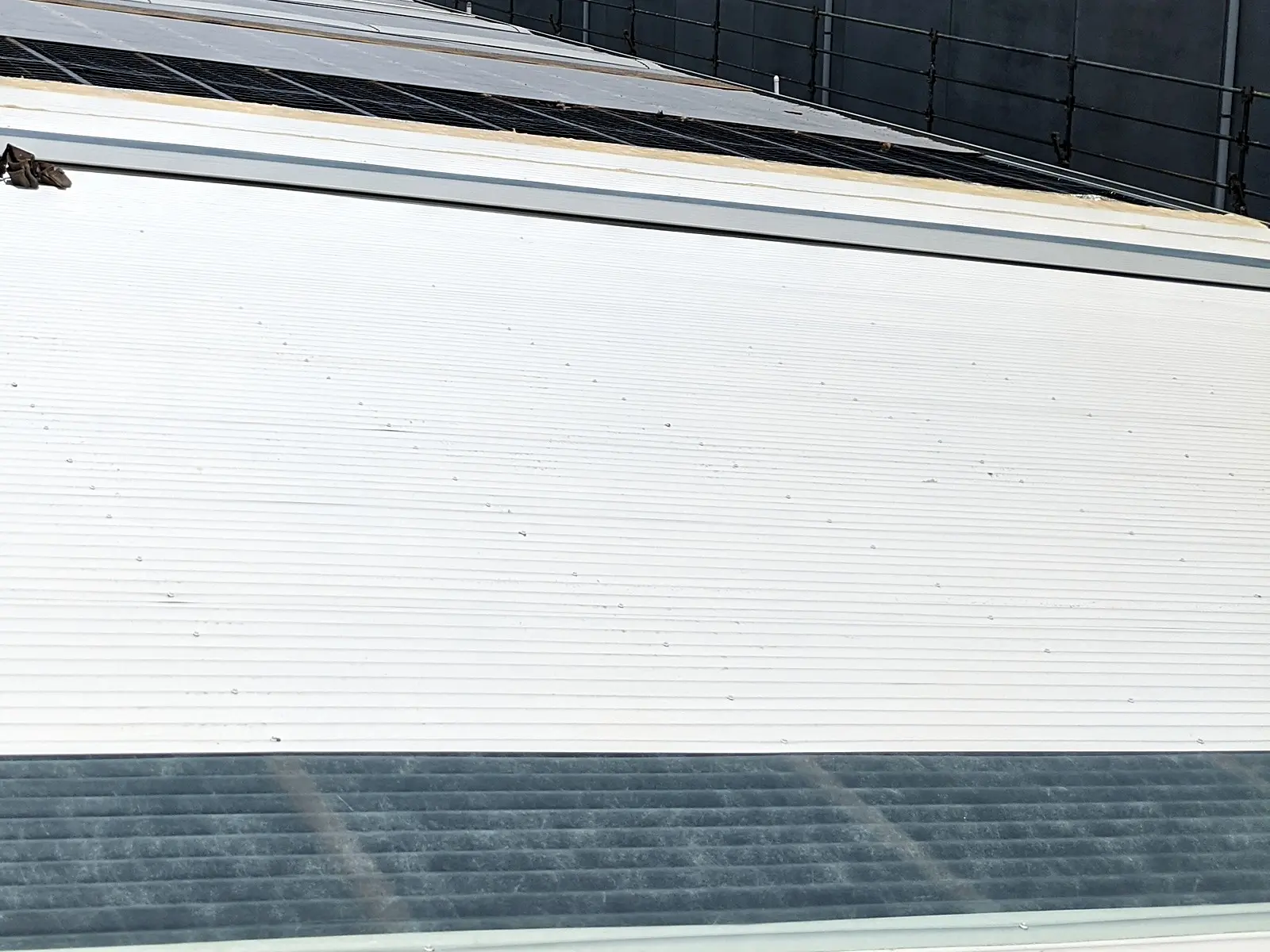 A new white metal roof with a run of skylight sheeting on an industrial building, solar panels beyond